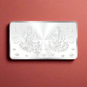 A rectangular 999 purity silver coin with two figures, Ganeshji and Lakshmiji, seated on a lotus design with floral patterns around it.